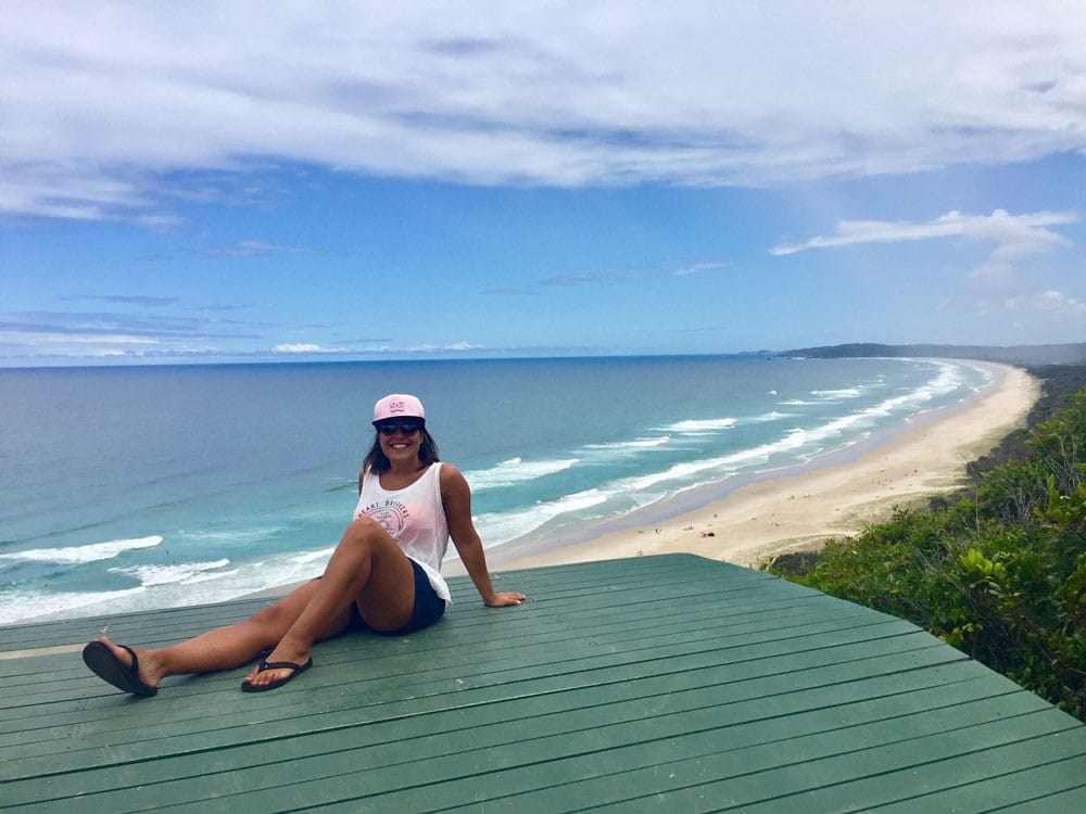 chica morena posando en un mirador de Byron Bay y detrás la playa